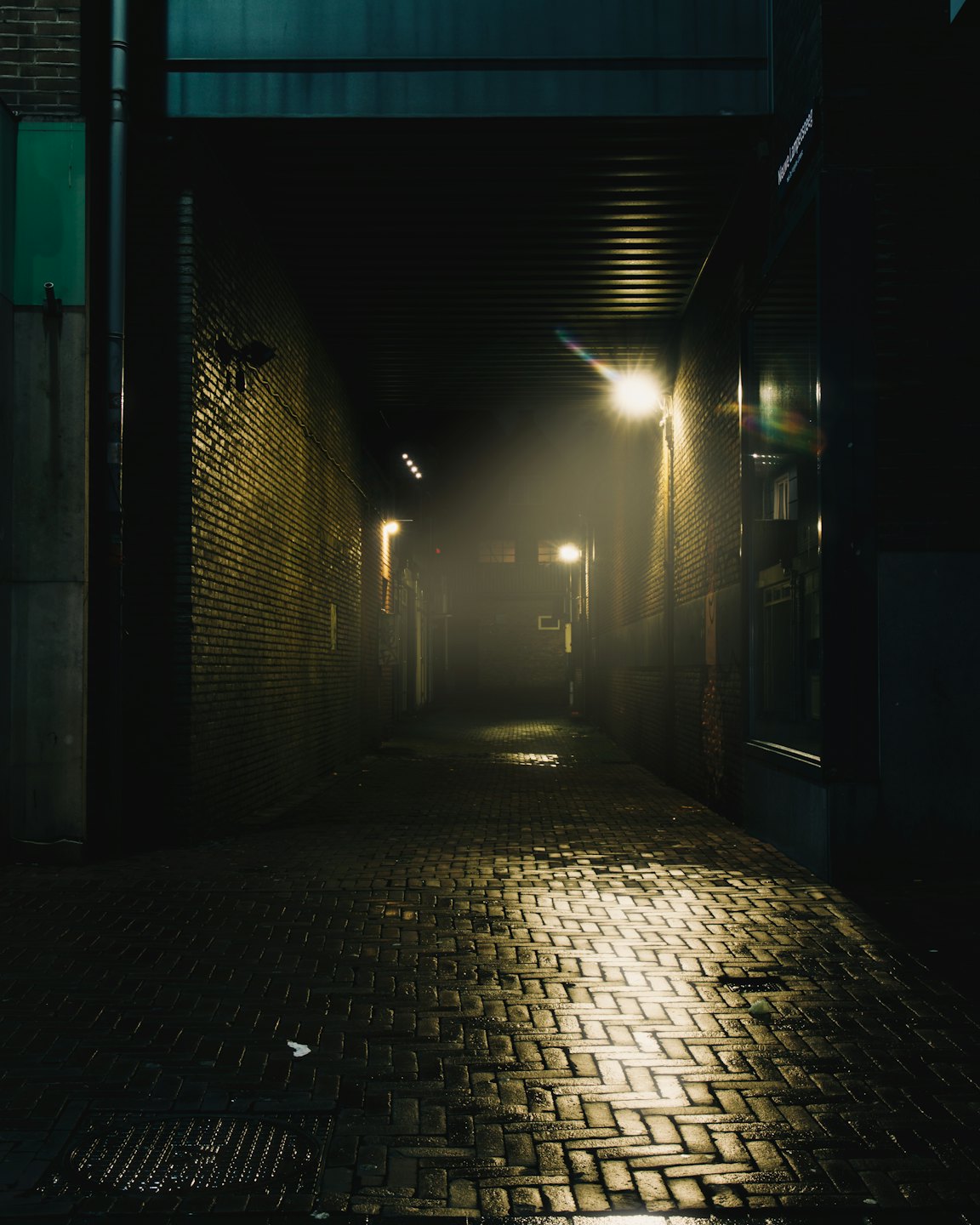 Nasse Kopfsteinpflastergasse bei Nacht mit gelben Straßenlaternen.