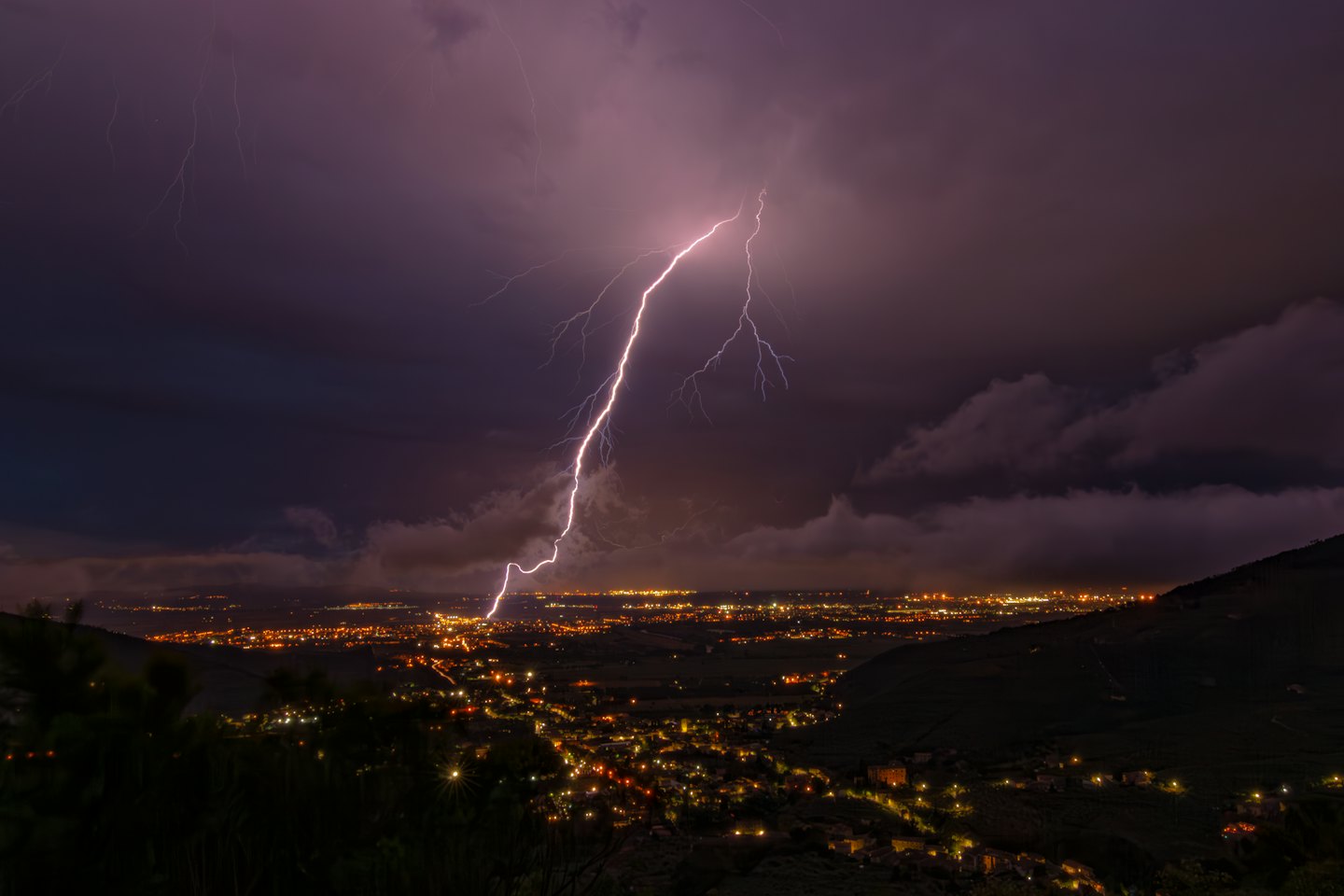 Ein Blitz schlägt über einer leuchtenden Stadt bei Nacht ein.